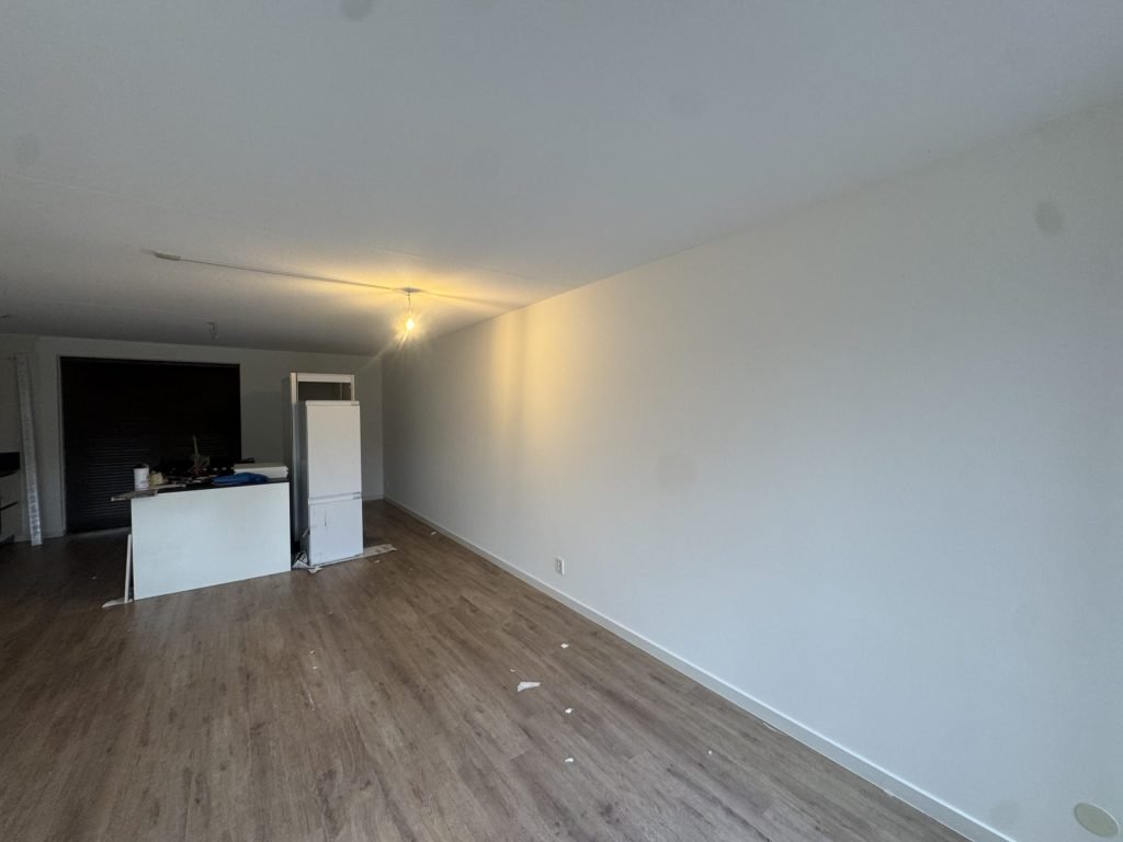 Lange strak afgewerkte witte wand in een nieuw appartement met open keuken en laminaatvloer