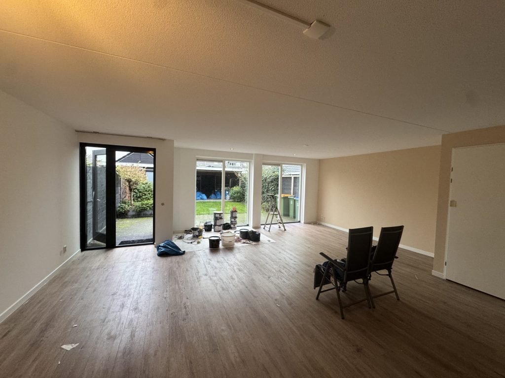 Lege woonkamer met lichte wanden, verfemmers en een trapje bij de tuindeuren, klaar voor de behanger